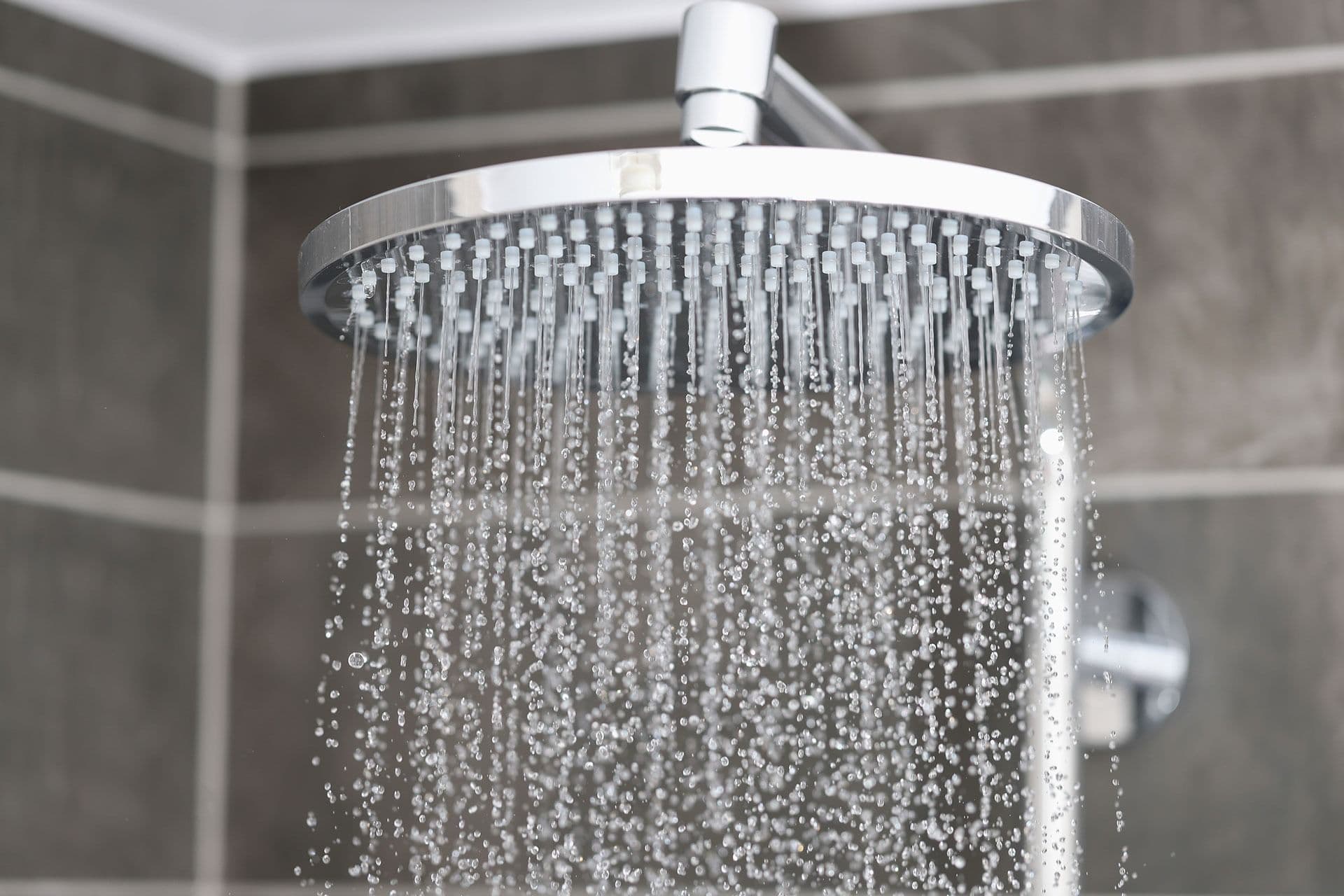 Close-up of a modern chrome shower head with water streaming down amidst tiled bathroom walls.