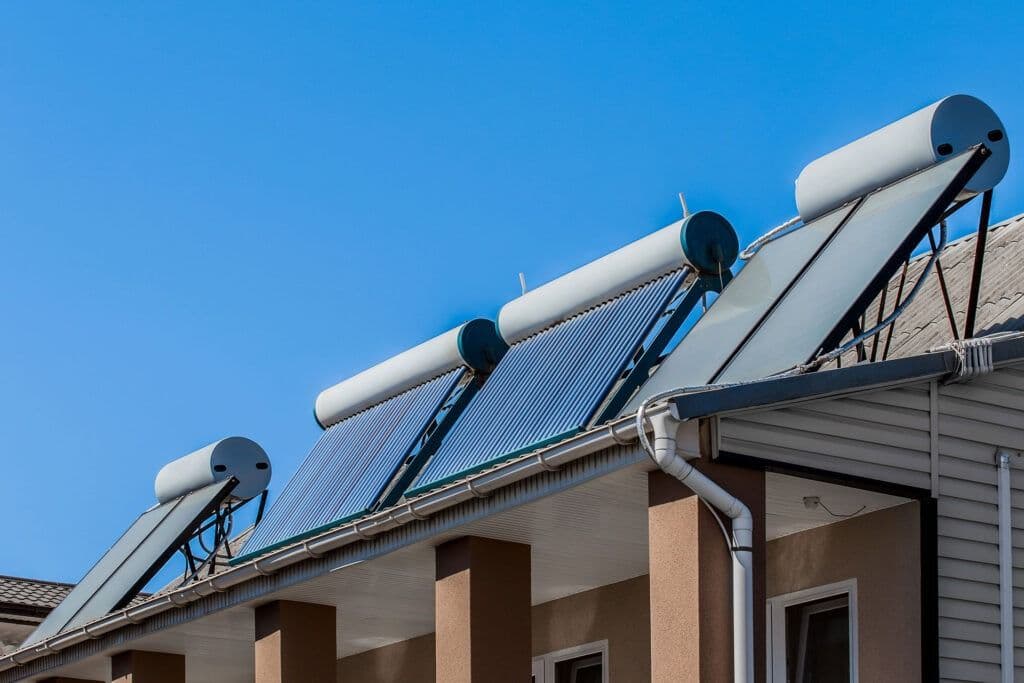 Rooftop solar water heaters with cylindrical tanks and solar panels are installed on a modern house, under a clear blue sky.