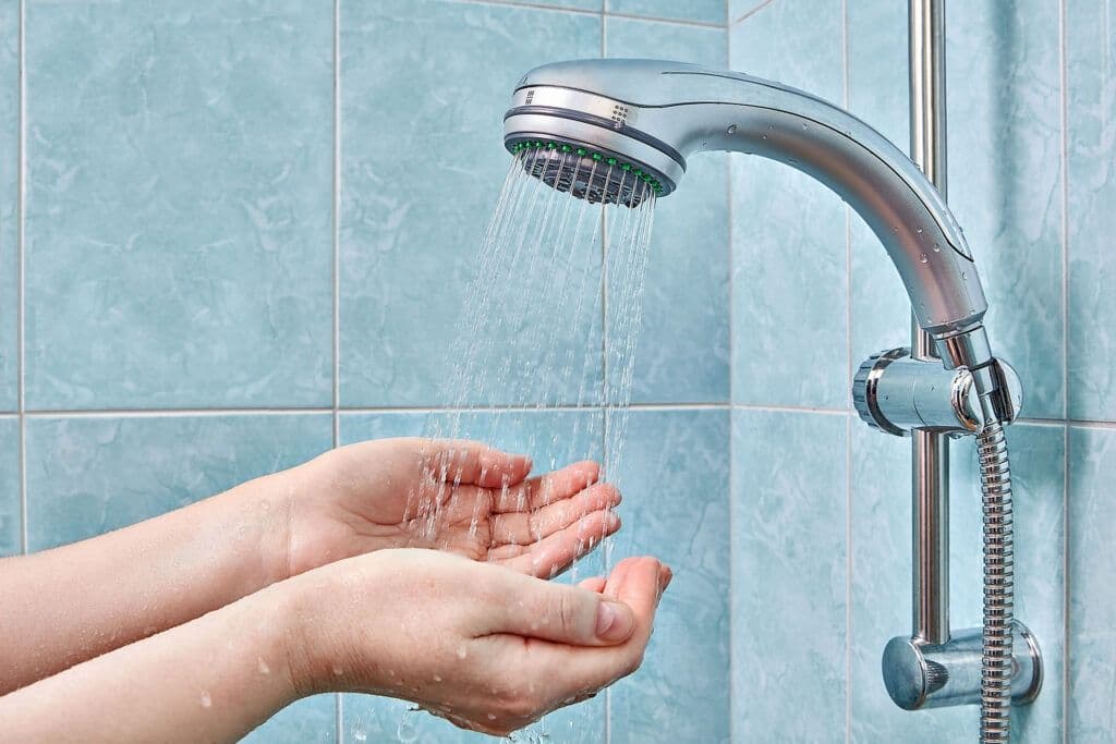 A person holds their hands under a showerhead in a blue tiled shower.