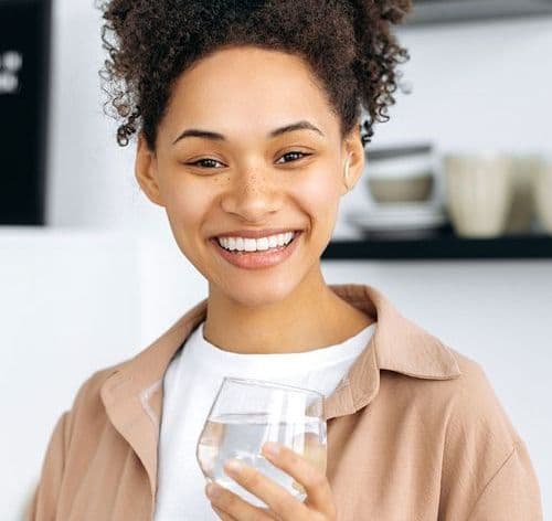 A person smiles and holds a glass of water.